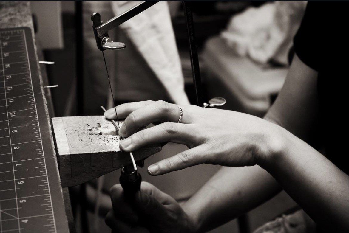 Black-and-white photo of hands sawing metal at the jeweler’s bench