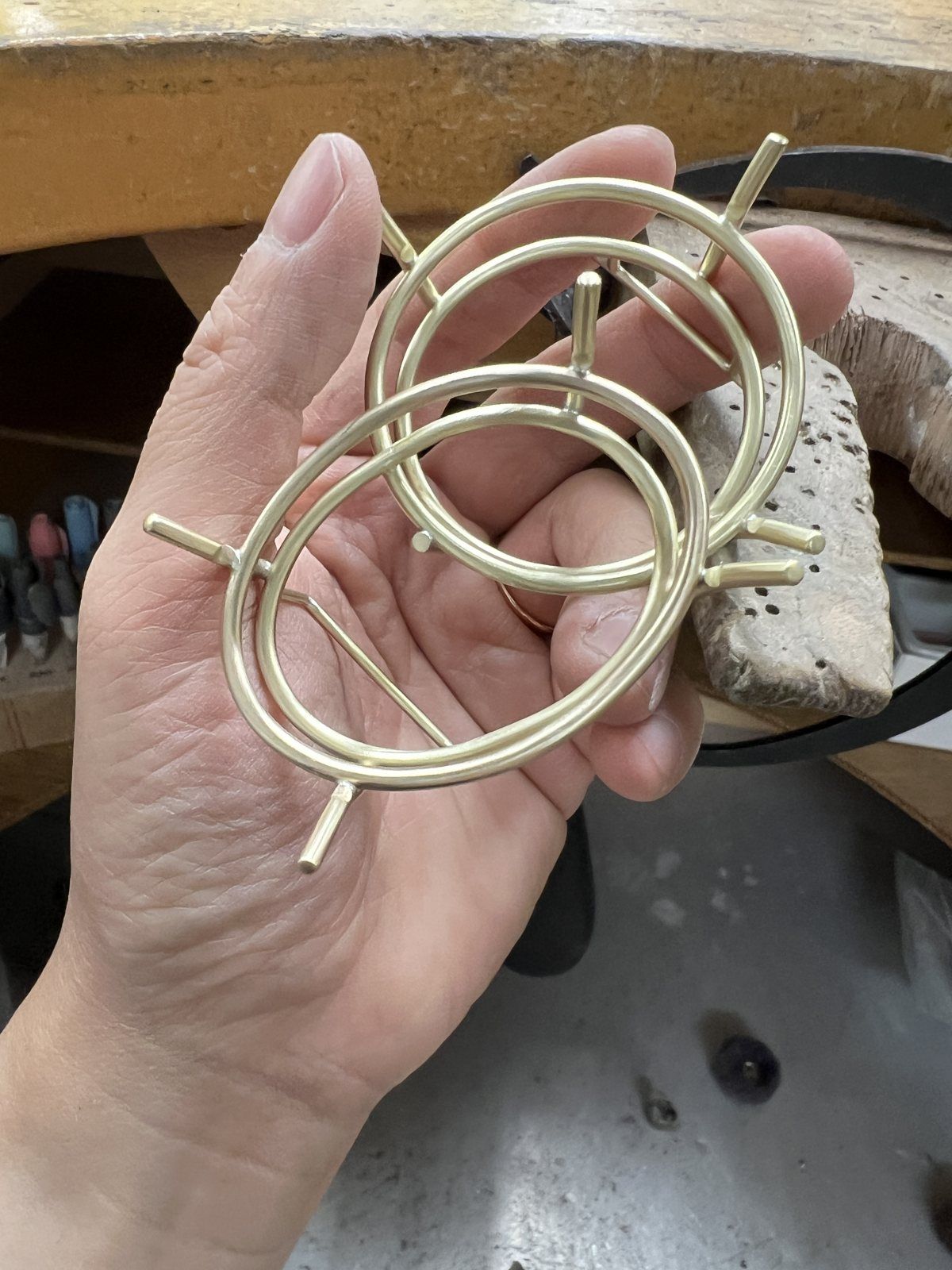 A hand holding two brass oval frames with prongs