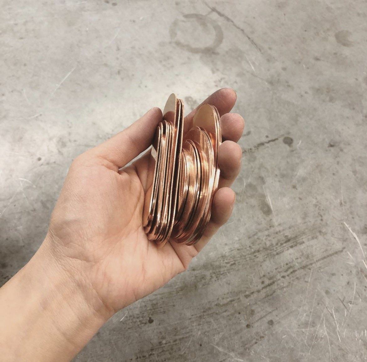 A hand holding a stack of cut copper pieces