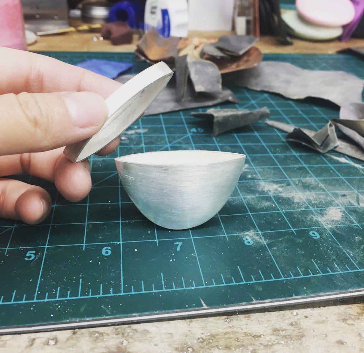 A domed silver form and disc held over a cutting mat