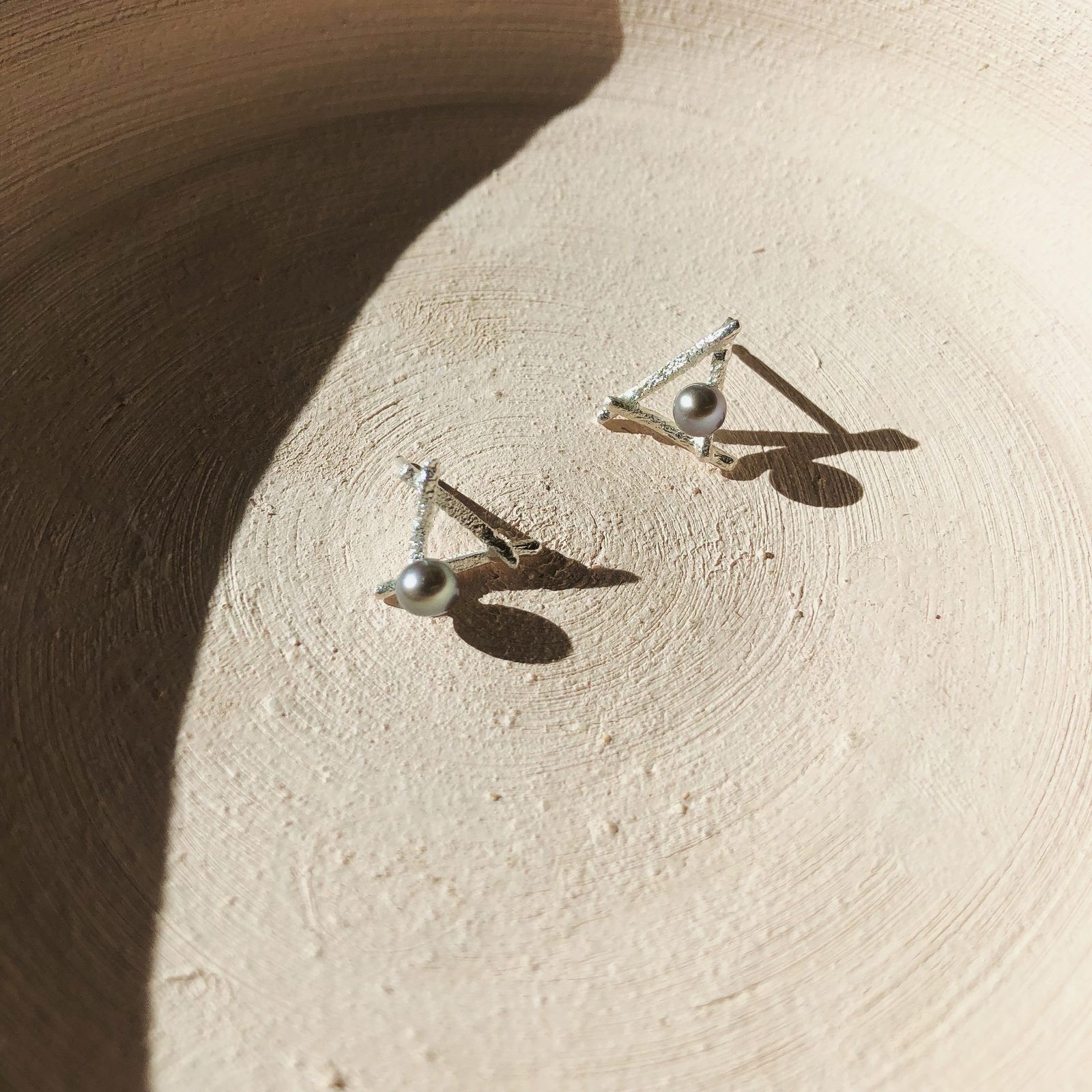 Silver triangle studs with grey pearls on a cream plate