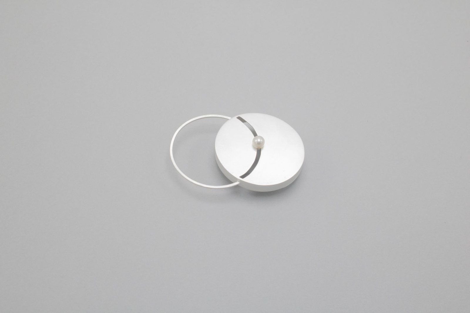 Silver brooch: an open circle beside a solid disc with a single pearl