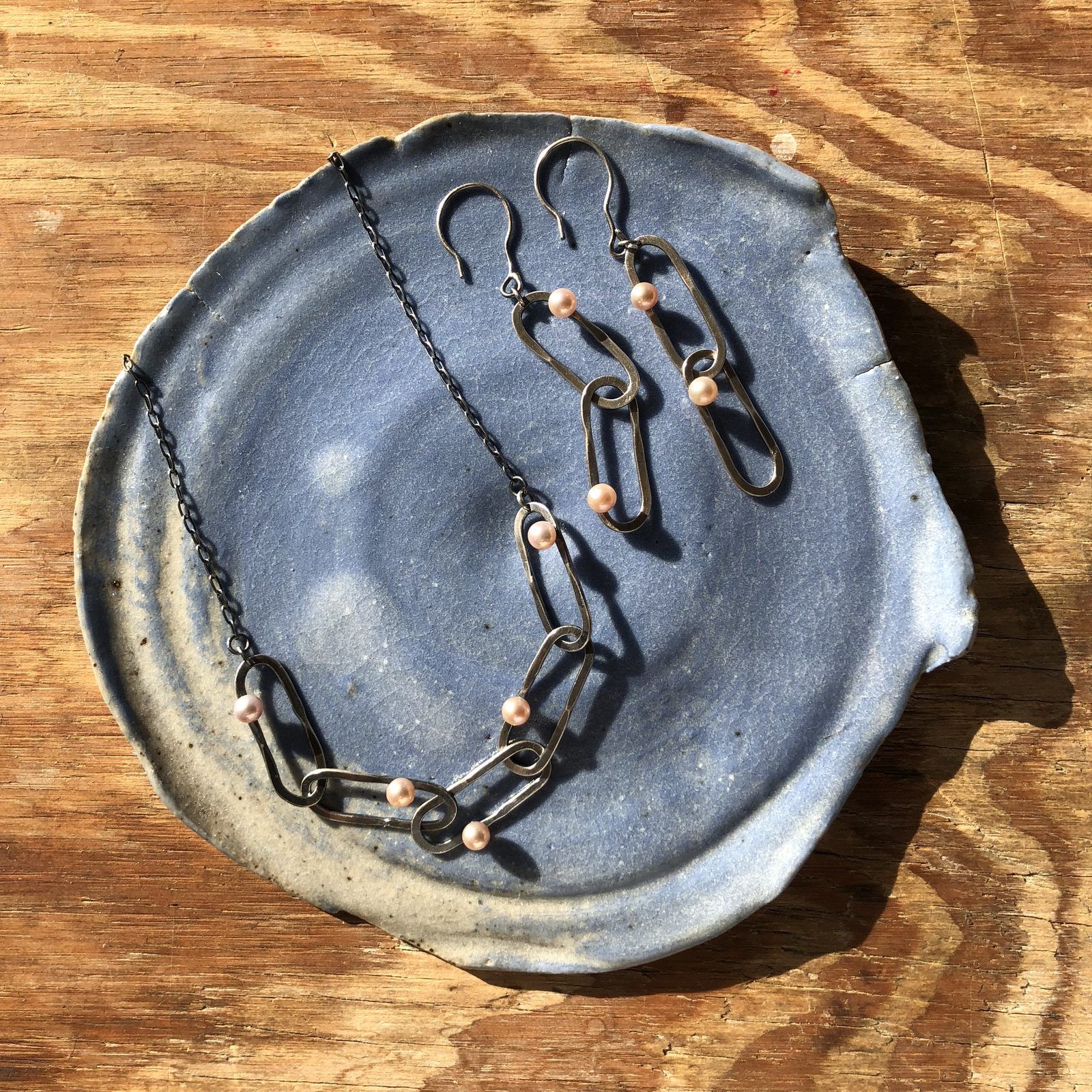 A matching link necklace and earrings with small pearls, on a blue ceramic dish
