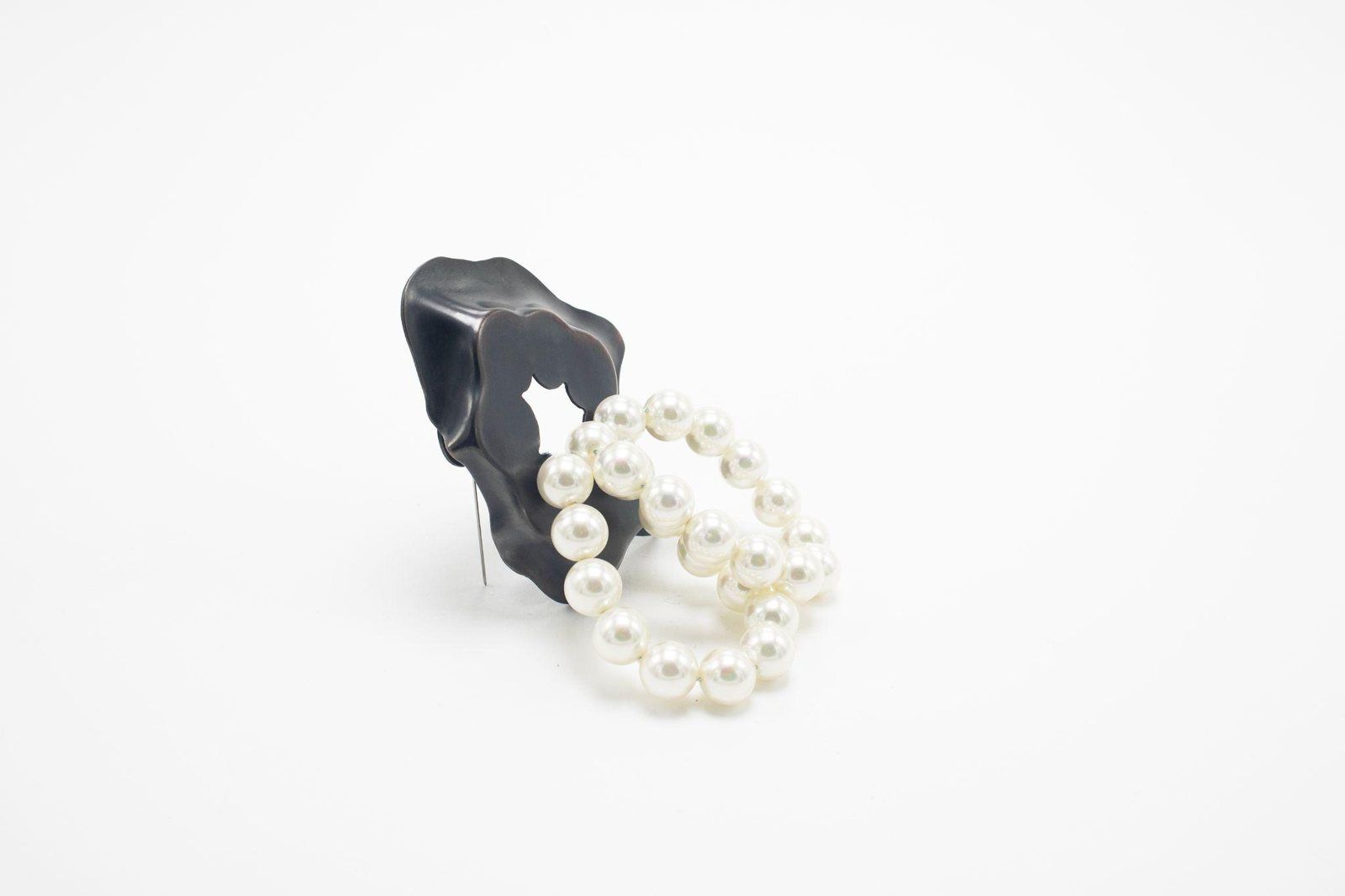 Dark folded copper form holding a loop of faux pearls