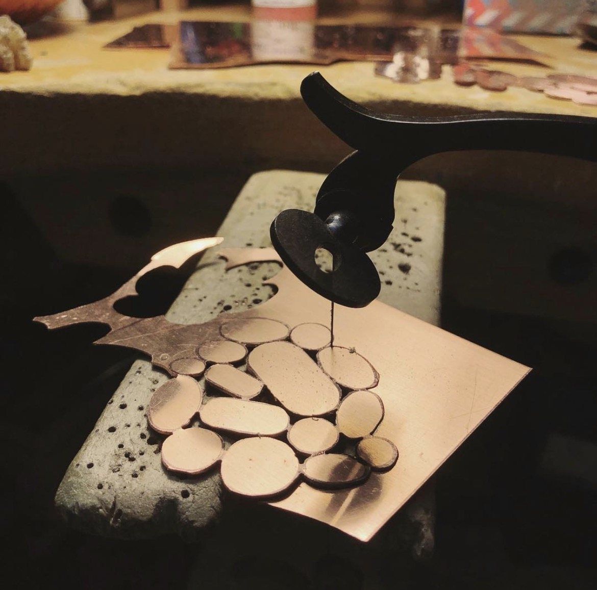 Copper sheet being pierced with a jeweler’s saw at the bench pin