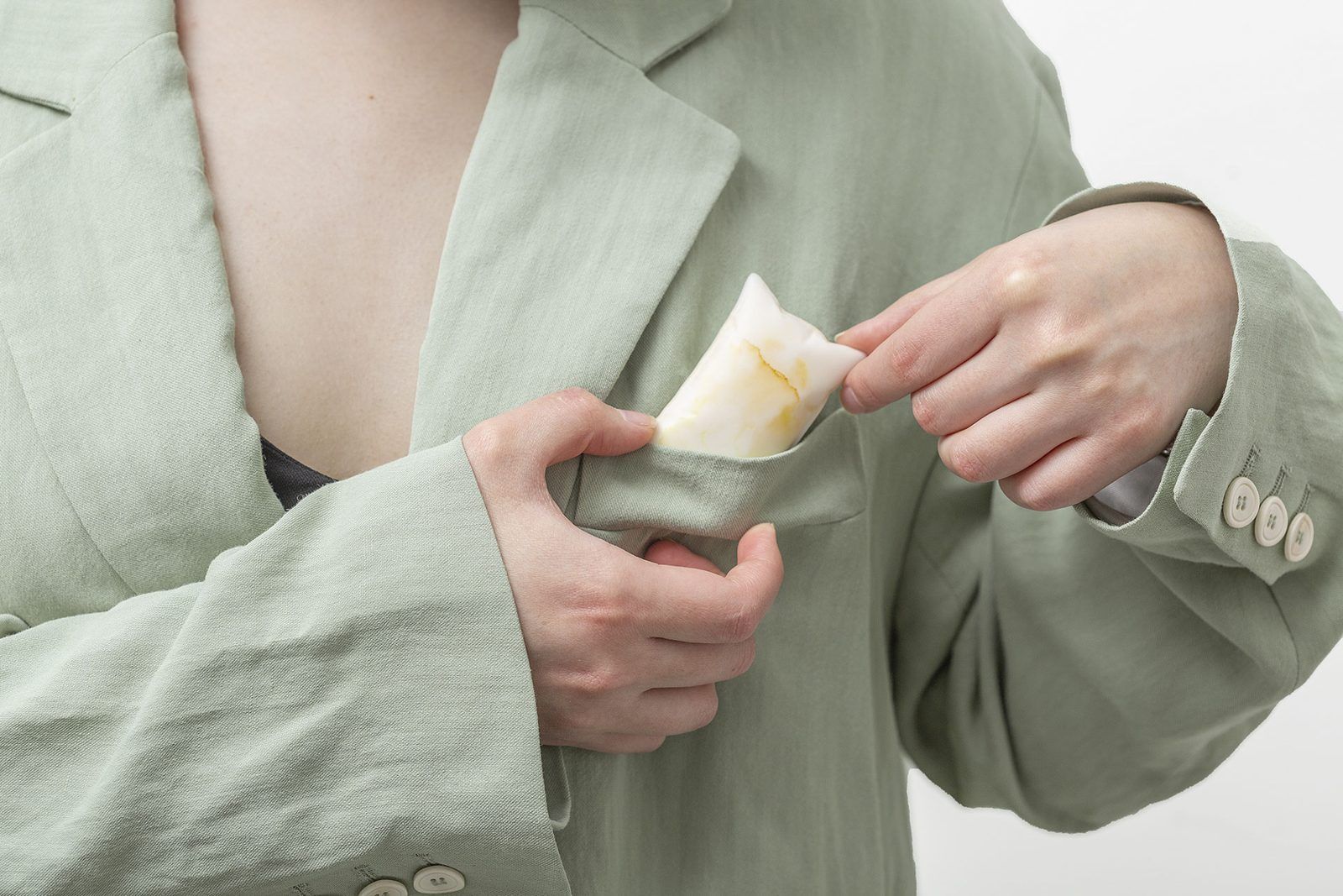 A woman tucks a small white pillow pendant into the pocket of her sage linen jacket