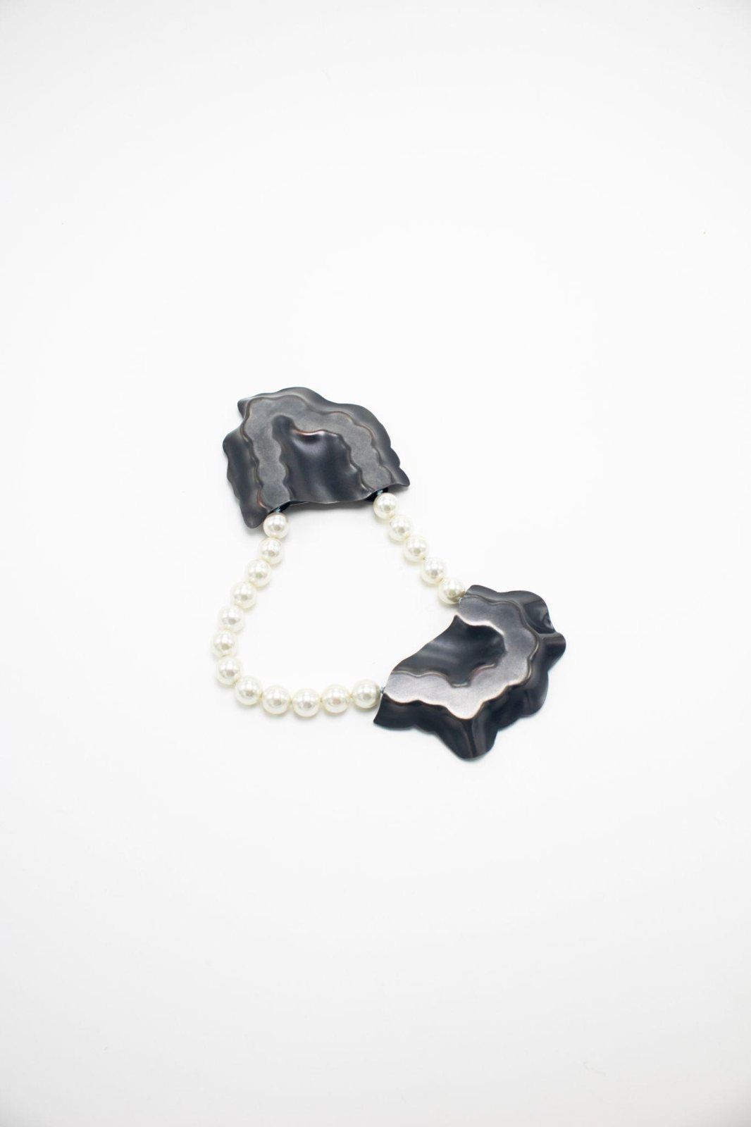 Two dark folded copper forms joined by a strand of faux pearls