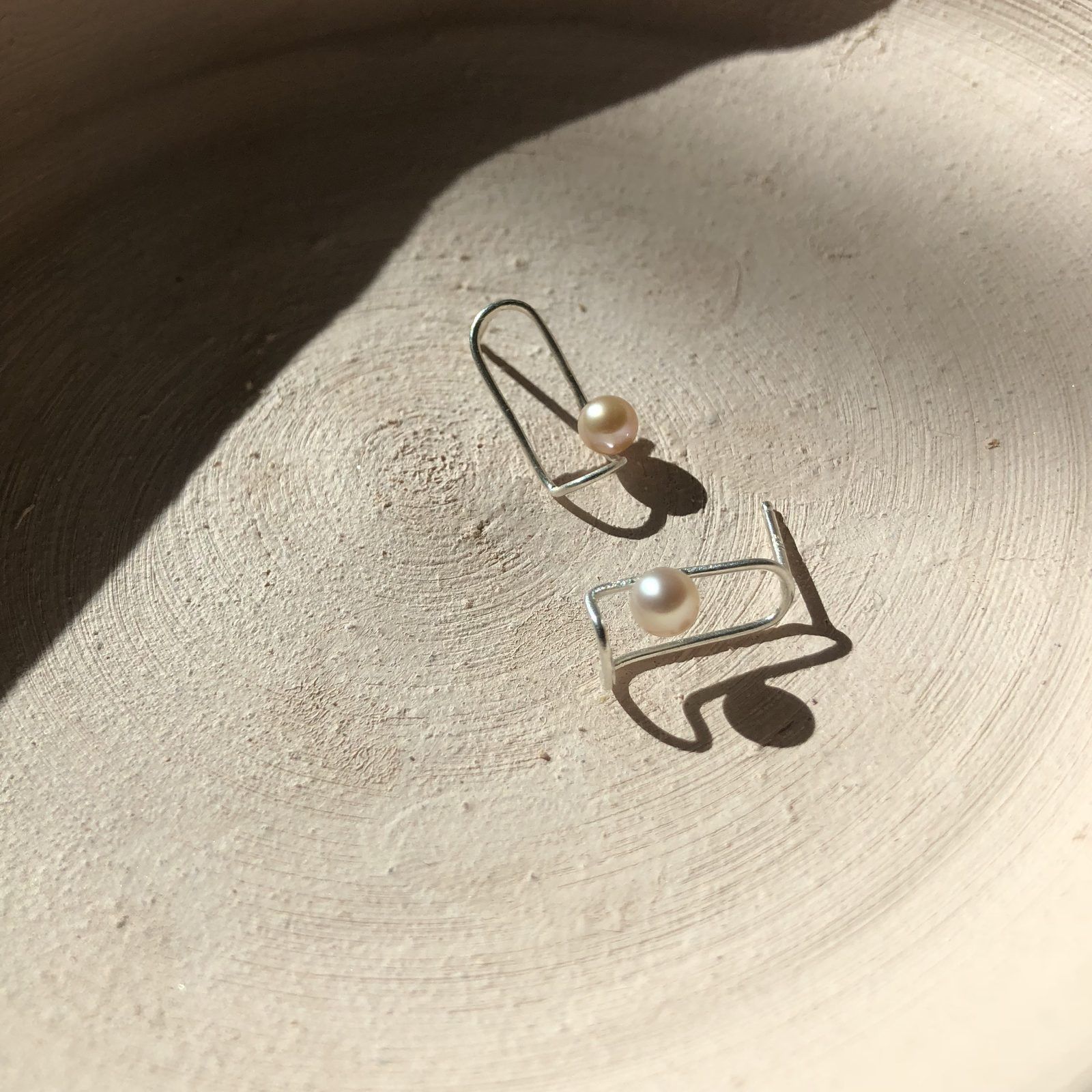 Silver wire loop earrings with small pearls, in sunlight on a cream plate