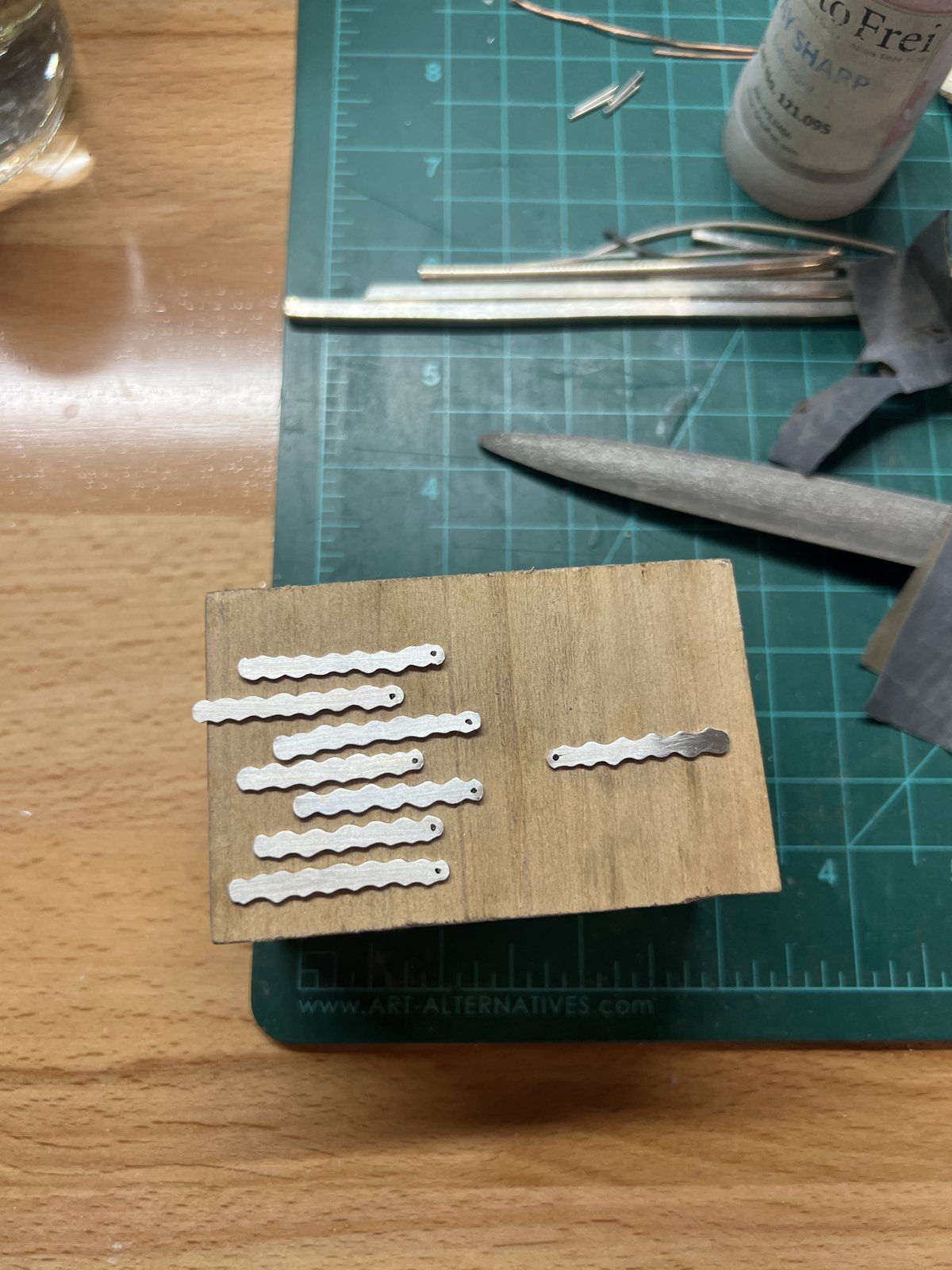 Small cut silver strips laid out on a wooden block at the bench