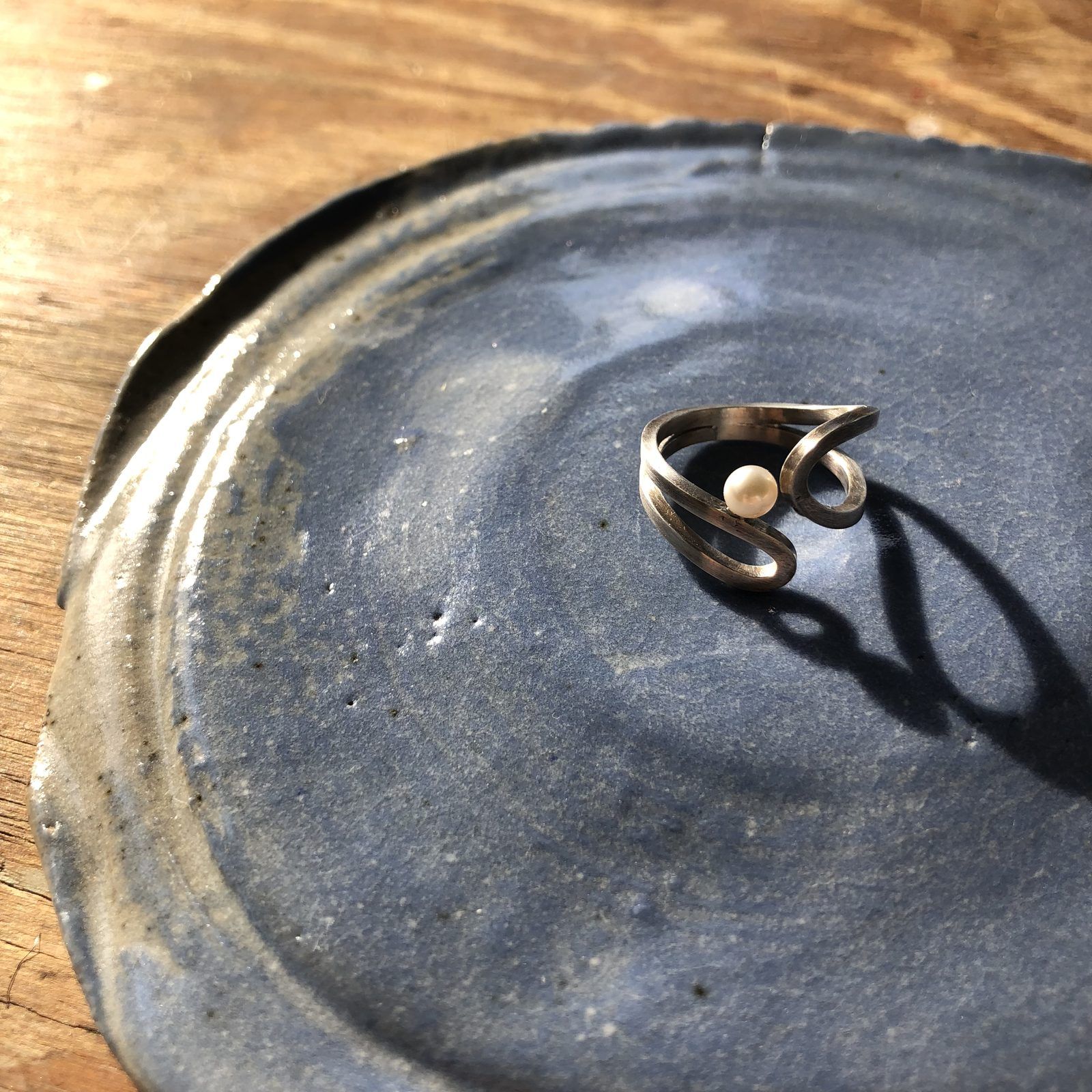Oxidized silver wave ring set with a single pearl, on a blue ceramic dish